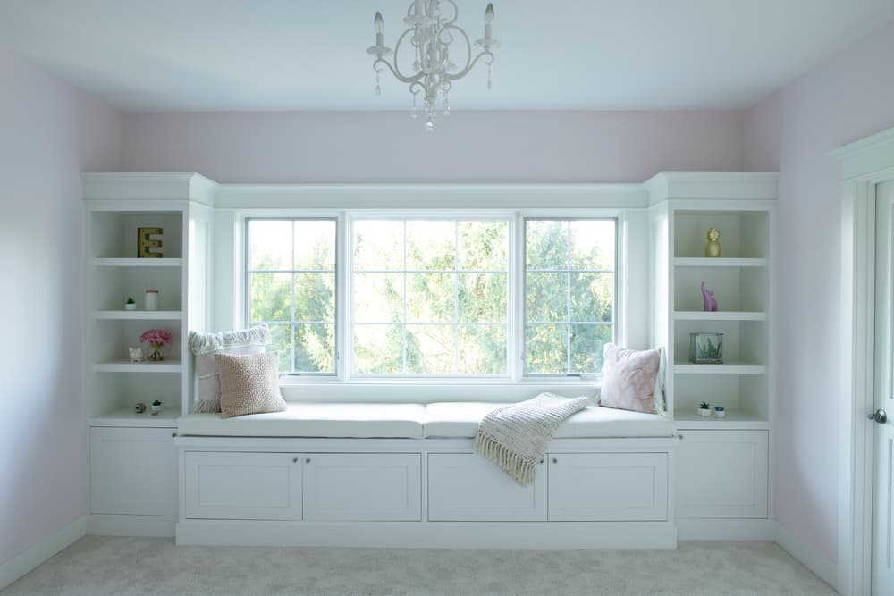 Picture Window Sheds Light On Cozy Window Seat Book cases surround white window seat in pink bedroom