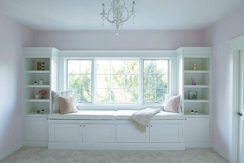 Picture Window Sheds Light On Cozy Window Seat Book cases surround white window seat in pink bedroom