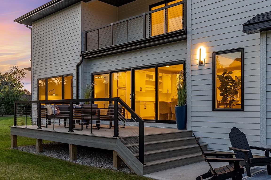 Backyard deck with contemporary railing and large windows glowing in evening light.