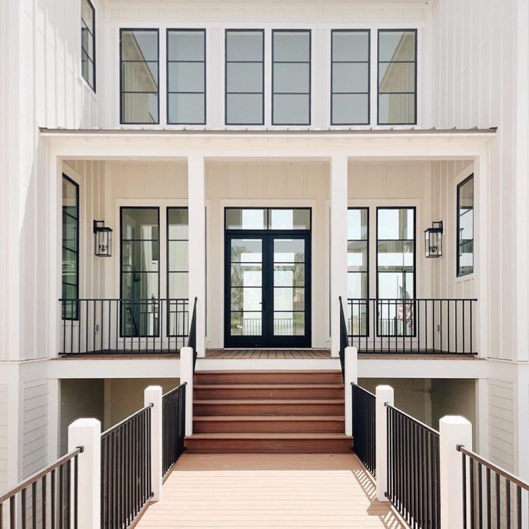 The exterior of a white home has modern French doors and black windows overlooking the front porch.