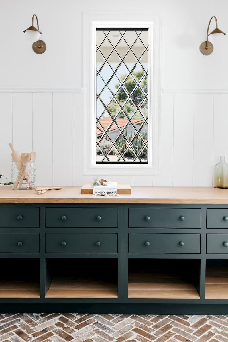 Green cabinets and a wood countertop sit below a custom window with diamond panes in this kitchen.