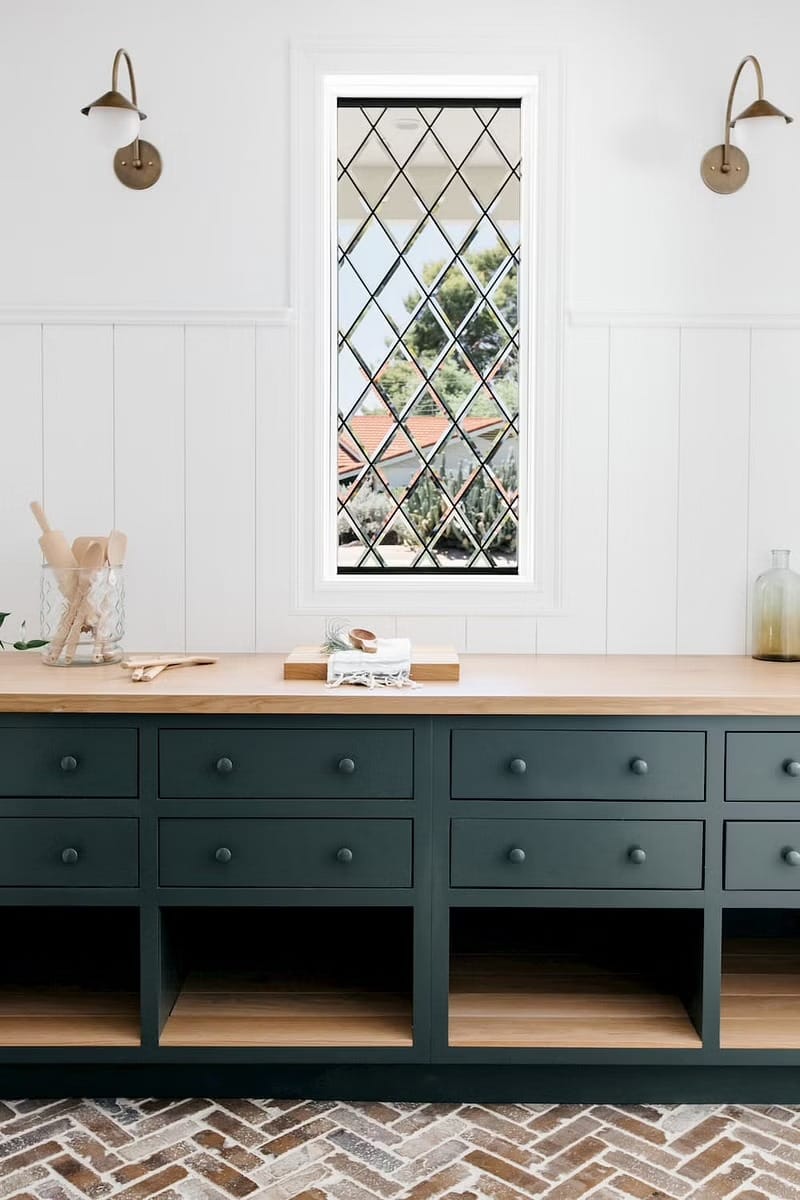 Green cabinets and a wood countertop sit below a custom window with diamond panes in this kitchen.
