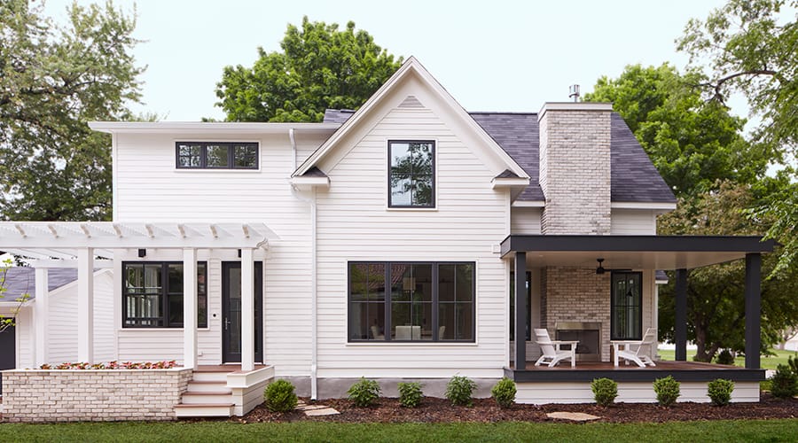 A white farmhouse-style home with black windows and a black-painted front deck.