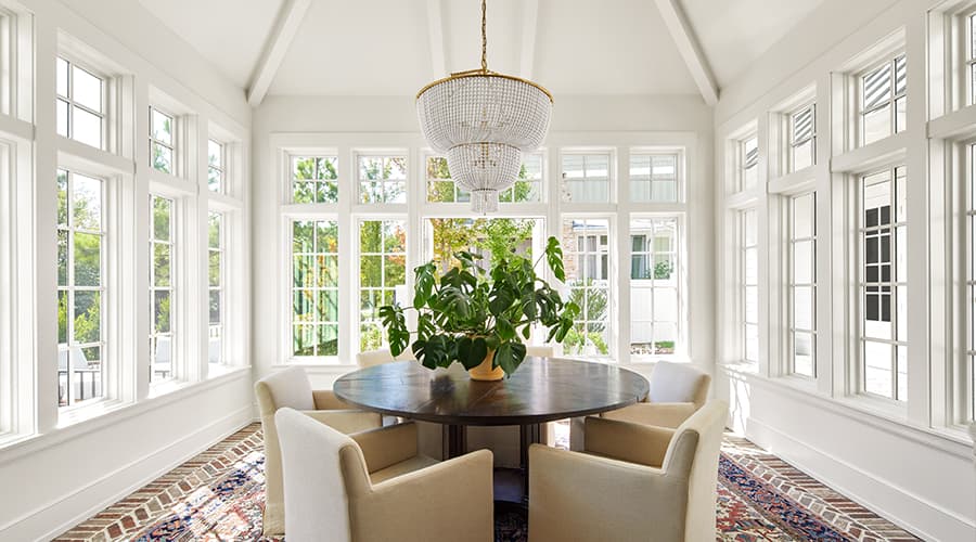 Five beige armchairs around a circle table that sits in the middle of a room that has windows on every wall.