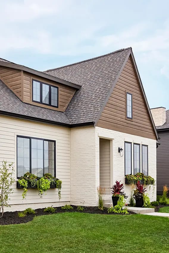 Modern house exterior with brown gable roof, beige siding, window flower boxes and landscaped lawn