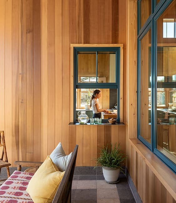 Looking through a green window to see a woman working in her kitchen.