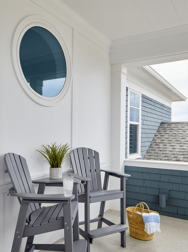 a circle window on the wall of a deck with two deck chairs below