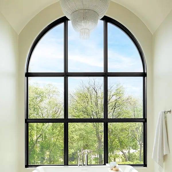 Large arched window with black grilles overlooks trees, above a bathtub in a bright bathroom.