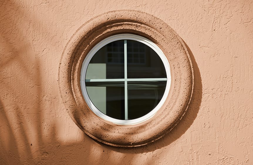 Round white trim window in a bathroom with a black grille
