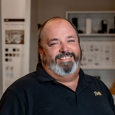 A man with a gray and black beard is wearing a black Pella shirt and smiling at the camera.