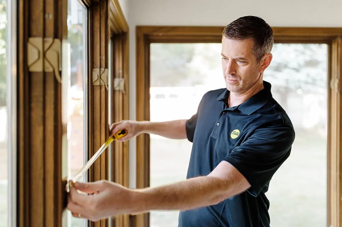 Worker measuring a wooden window frame with a tape measure for home window installation