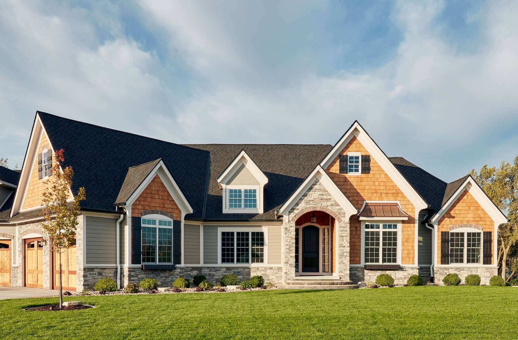 A brick and tan home exterior featuring white-framed windows and a well manicured lawn.