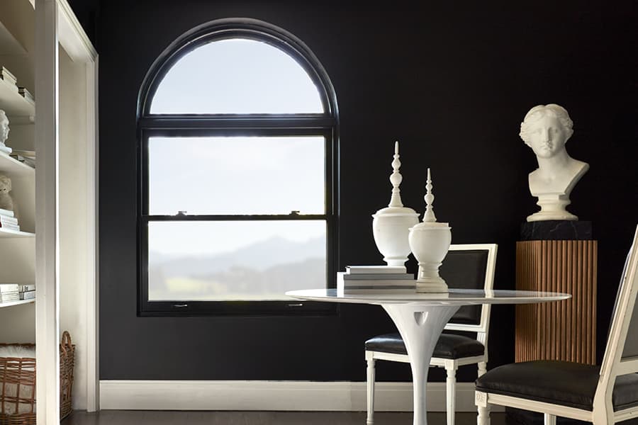 Black double-hung window with transom next to a white bust, bookshelf and table