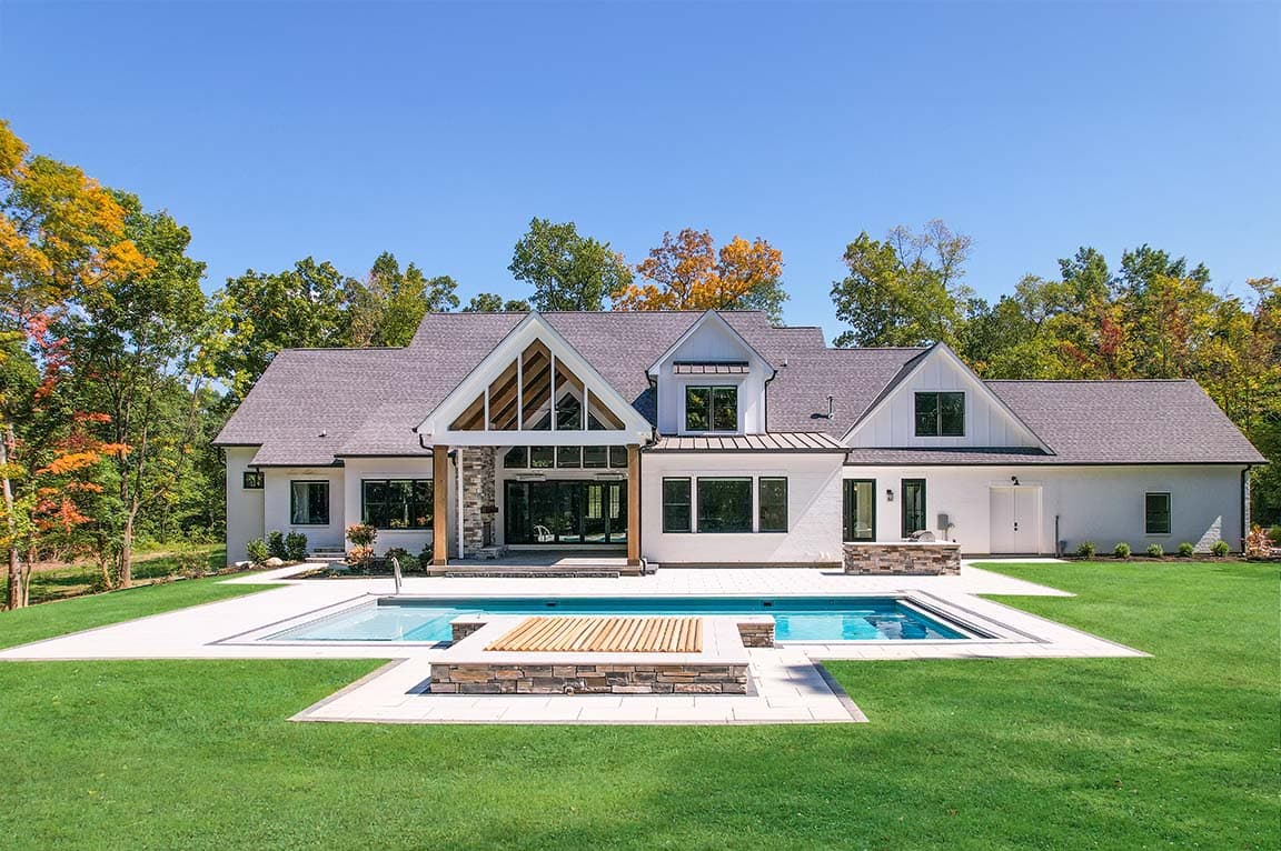 Modern white home with gable roof, large windows, covered patio, and backyard swimming pool.