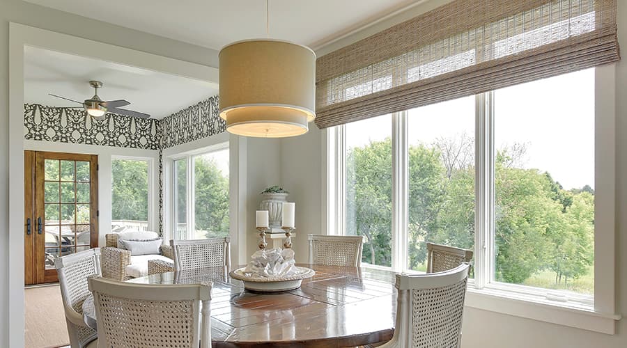 Round lights hang over a dining room table with large white windows along the exterior wall.