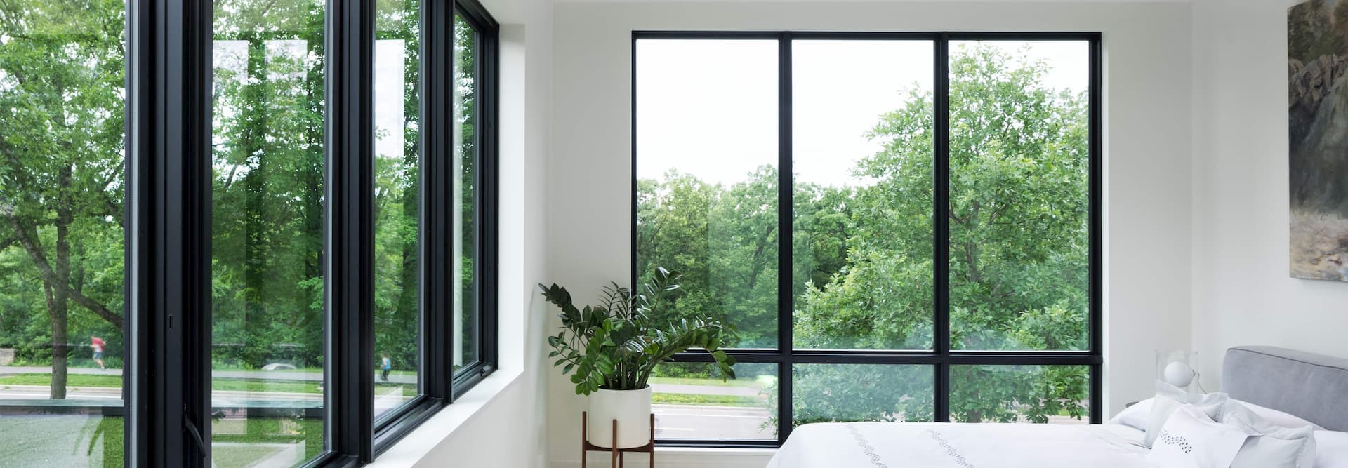 An all-white contemporary bedroom with three floor-to-ceiling windows bring the green trees into view.