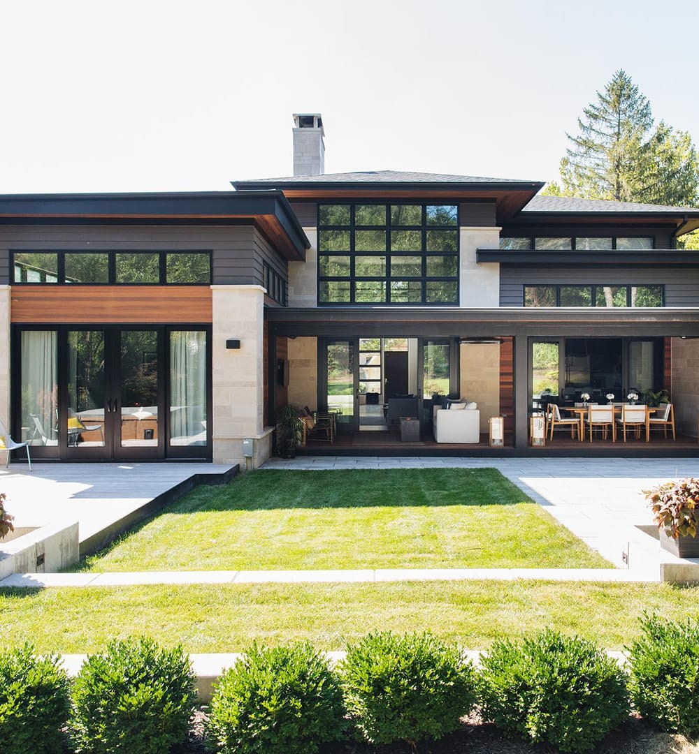 Modern and contemporary home features sliding patio doors and picture windows creating walls of glass across the back of the house.