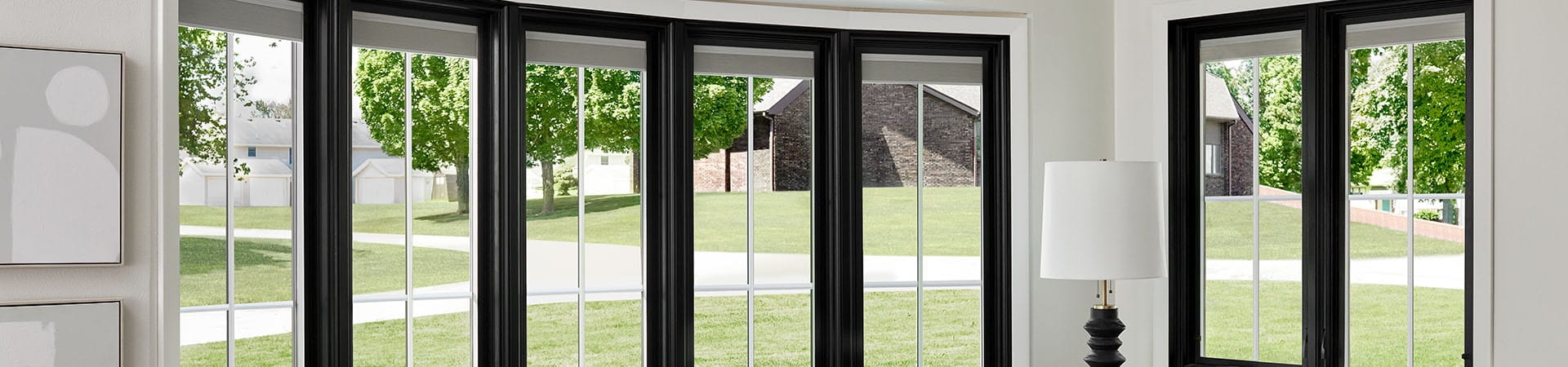 A modern living room featuring a black-framed bow window with a view of green trees and a house.