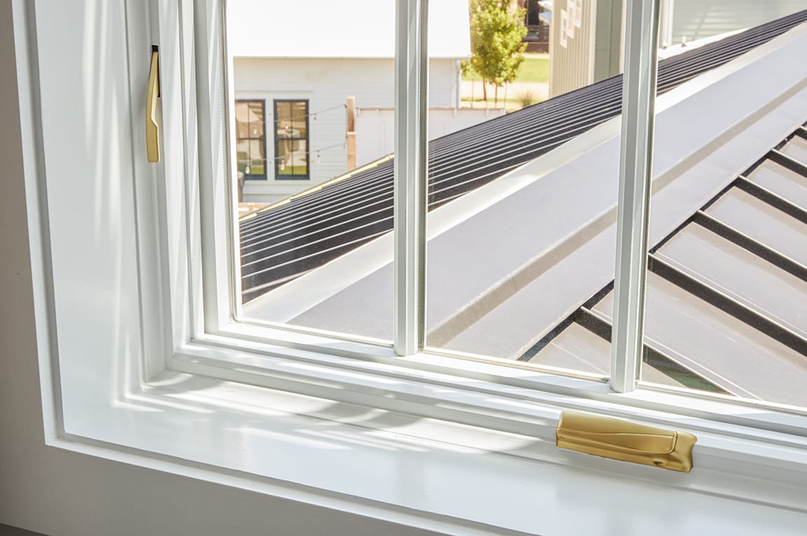 Close-up of interior window trim with a white frame and gold hardware, showcasing natural light.