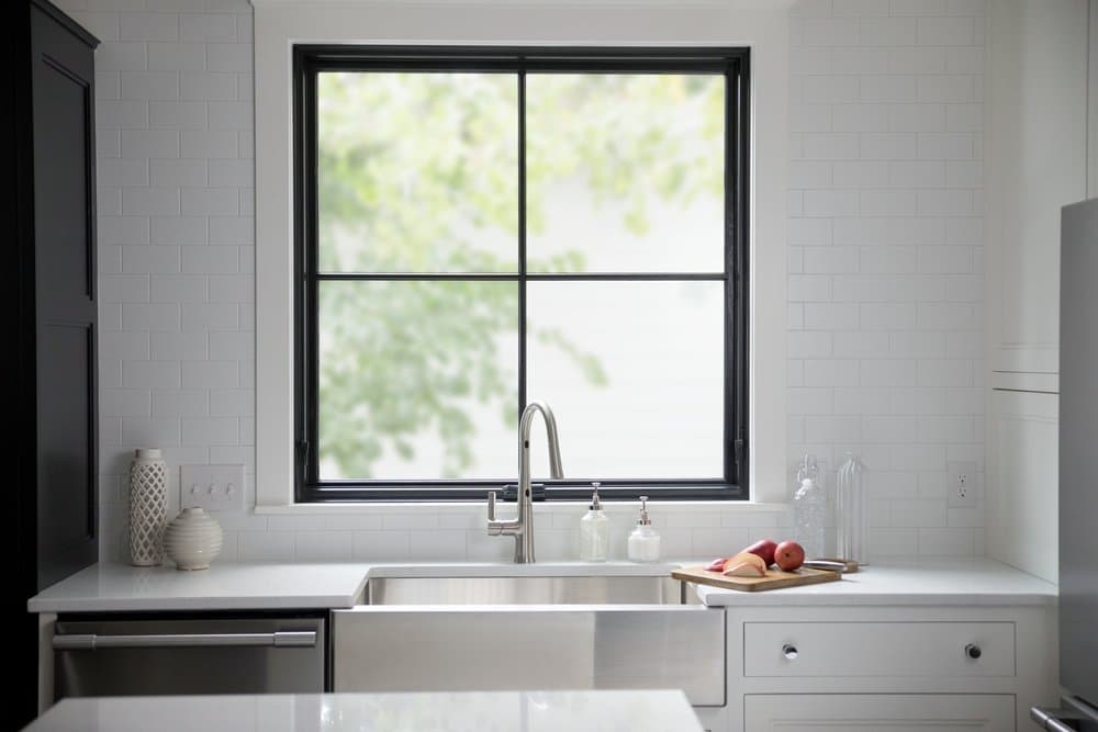 Square Window Creates Perfect Symmetry For Farmhouse Kitchen White kitchen counter with farmhouse sink and directly above it is a black square window design
