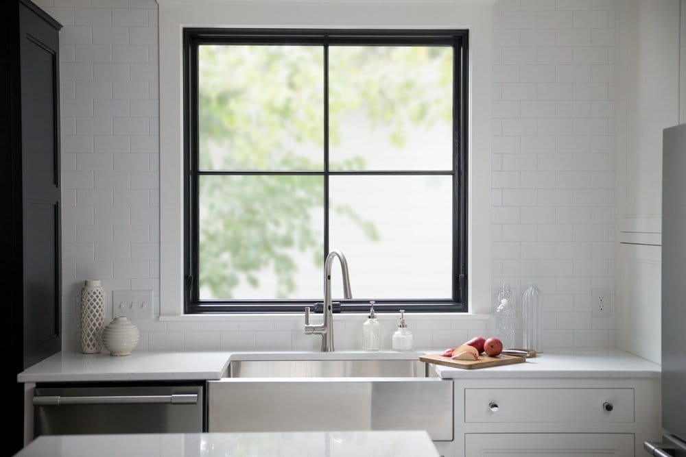 Square Window Creates Perfect Symmetry For Farmhouse Kitchen White kitchen counter with farmhouse sink and directly above it is a black square window design