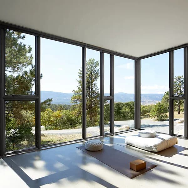 A serene room with combinations of large glass corner windows, meditation cushions, and a scenic outdoor view.