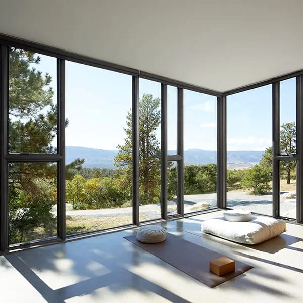A serene room with combinations of large glass corner windows, meditation cushions, and a scenic outdoor view.