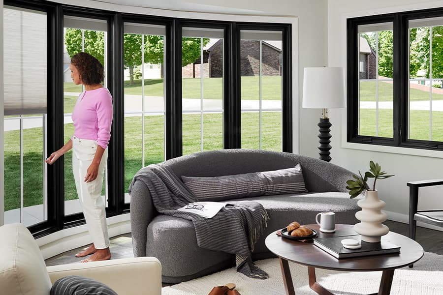 A woman is adjusting the shades on one window that's part of a five-window bay configuration.
