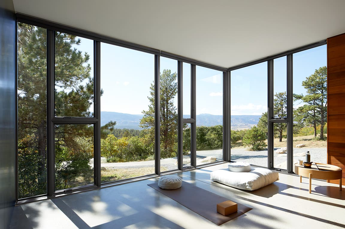 A serene meditation room with floor-to-ceiling windows overlooking trees and mountains, filled with natural light.