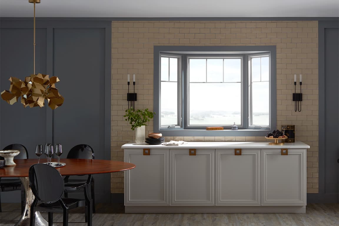 A modern kitchen featuring a bay window, gray cabinetry, and a wooden dining table.