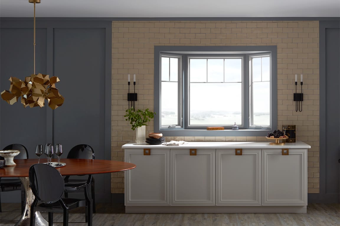 A modern kitchen featuring a bay window, gray cabinetry, and a wooden dining table.