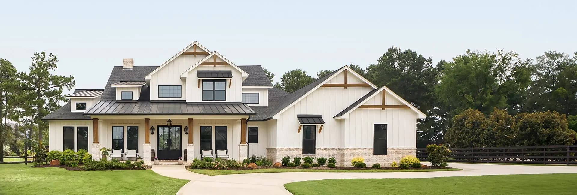 Modern two-story white farmhouse with black metal roof, covered front porch, landscaped yard and circular driveway