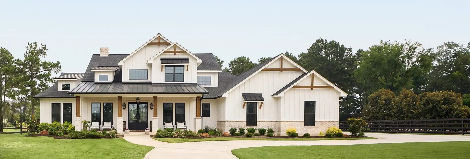 Modern two-story white farmhouse with black metal roof, covered front porch, landscaped yard and circular driveway