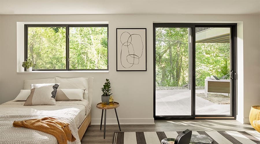 Black sliding door to the right of a black sliding window that is over a natural-colored bed.