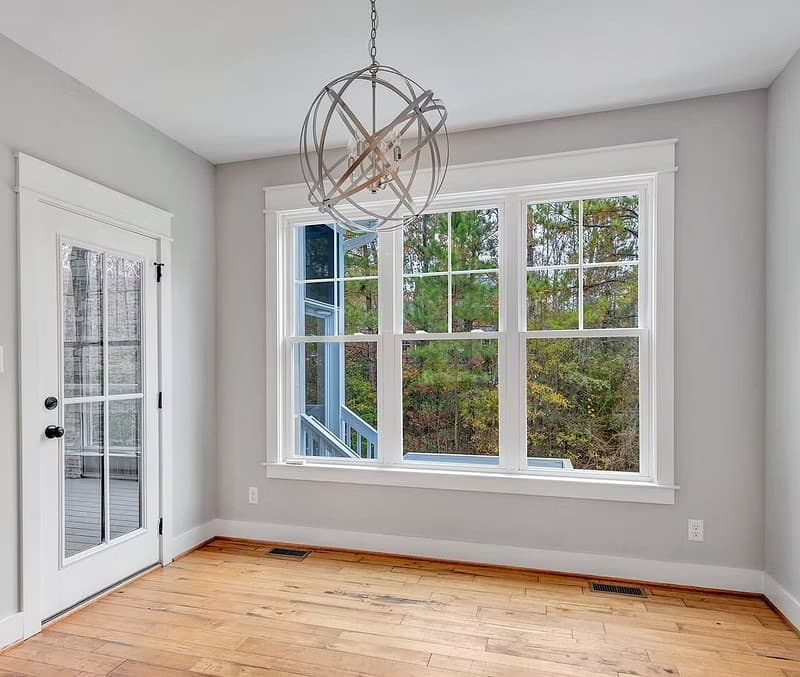 Home office has wood floors, gray walls, a chandelier and three white double-hung windows.