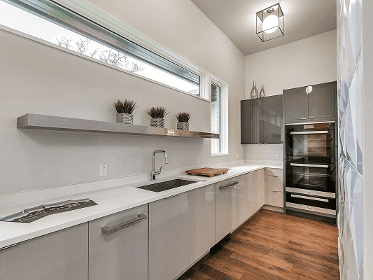 Rectangle Picture Window Brings Light Into Kitchen White on white long galley kitchen with cabinets along the wall and a long rectangle shaped window overhead