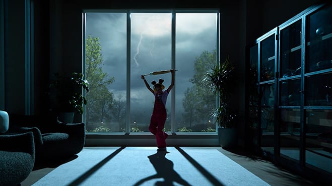 The silhouette of a small child dancing inside a dark house while it is storming outside the large windows.