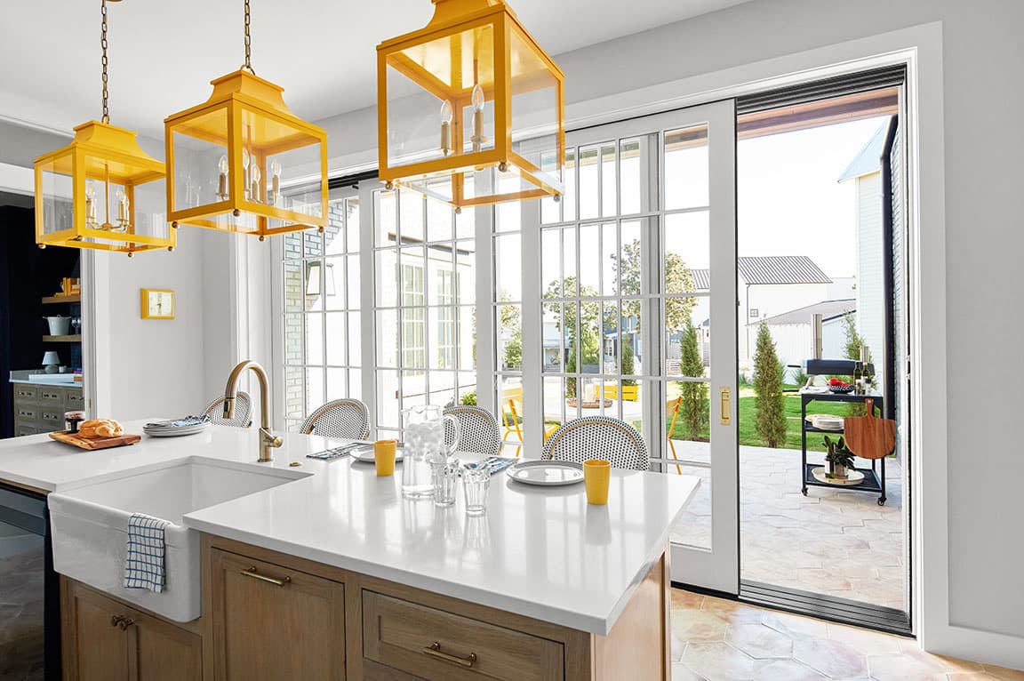 A modern kitchen with yellow lanterns, white countertops, and sliding doors leading to an outdoor patio, showcasing sliding door ideas.