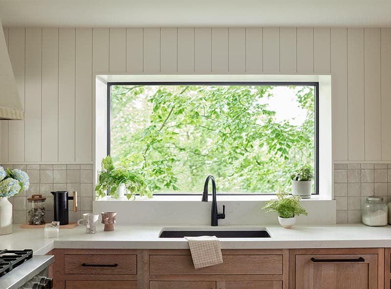 A modern kitchen featuring a black sink and a large garden window with greenery outside.
