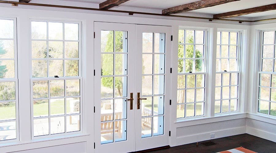 Four white double-hung windows with grilles sit to the left and right of a white french door with the same grilles.