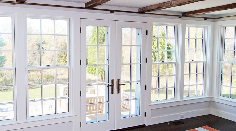 Four white double-hung windows with grilles sit to the left and right of a white french door with the same grilles.