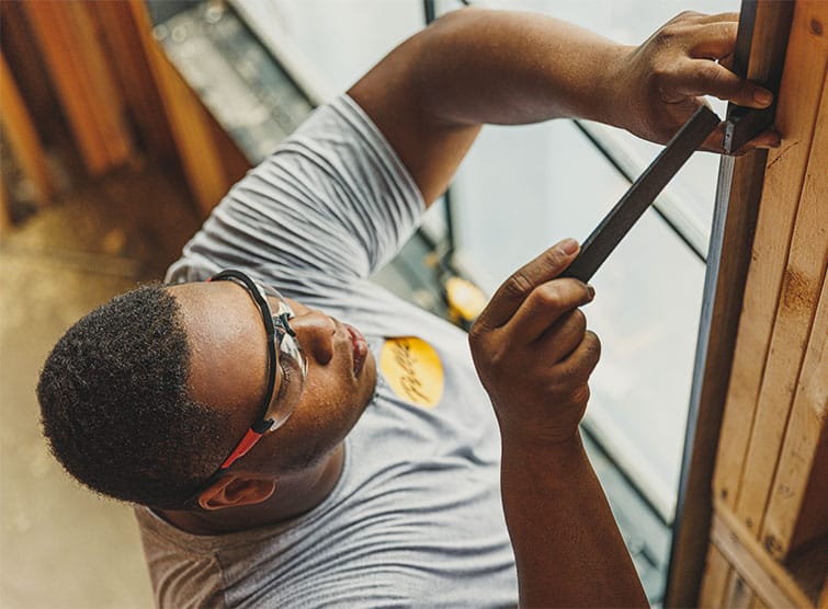 A man is using a tool to install a shim on a new window that's being installed into a new home.