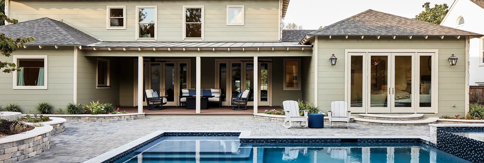 Backyard swimming pool and stone-paver patio with covered porch seating at a modern home