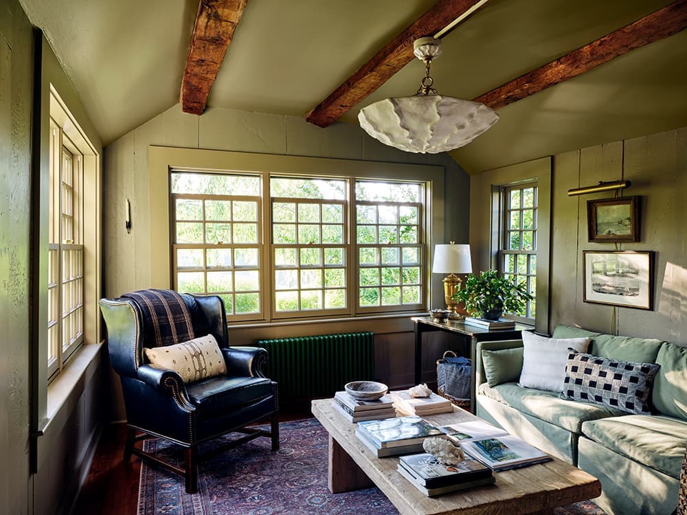 A traditional living room with three large almond double-hung windows and a green radiator below them.