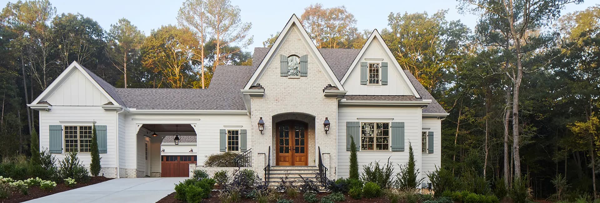White modern farmhouse with gabled roof, wooden double front door, blue shutters, attached garage and landscaped front yard