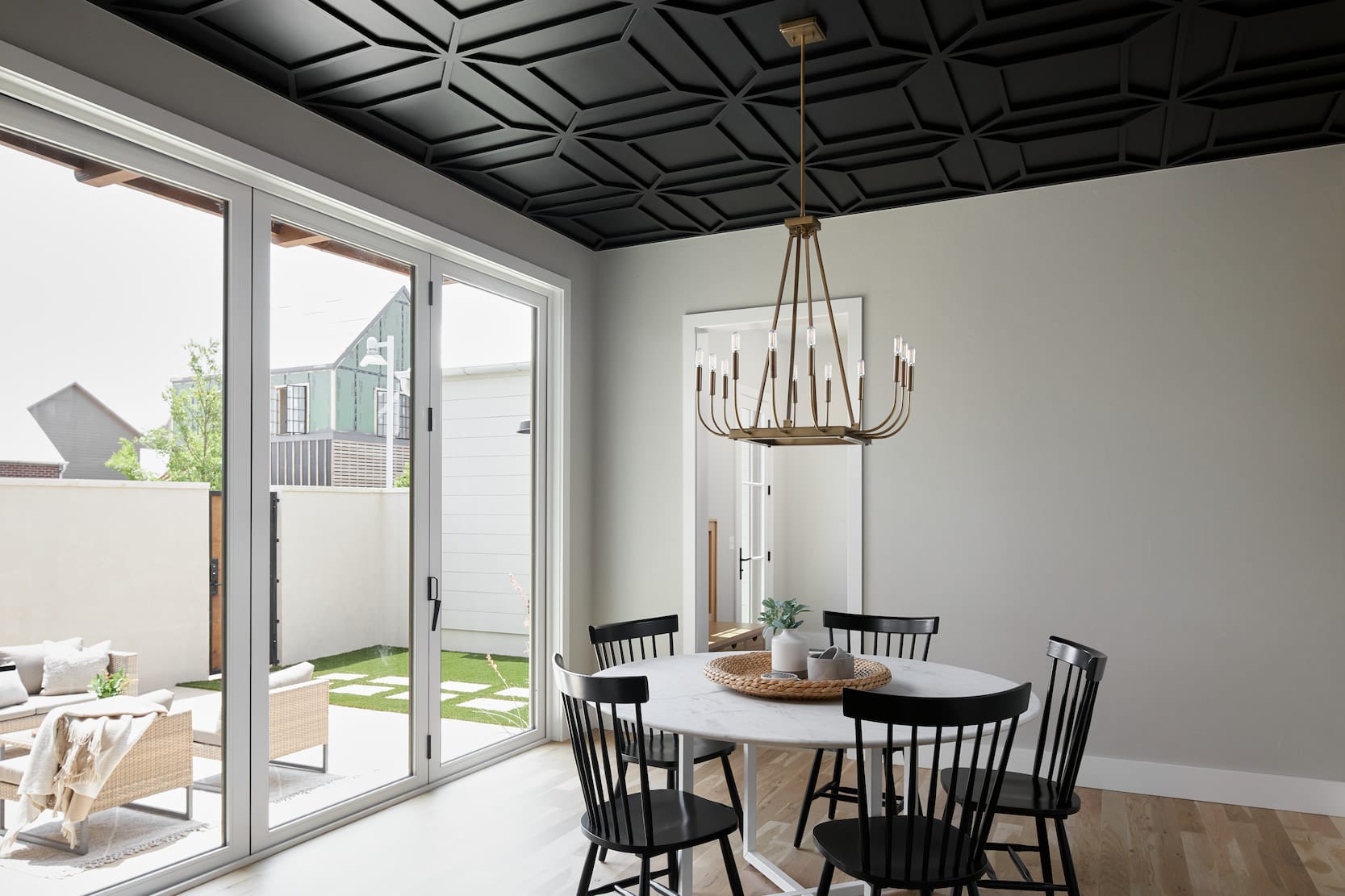 A dining room with a round table and black chairs features a white bifold patio door.
