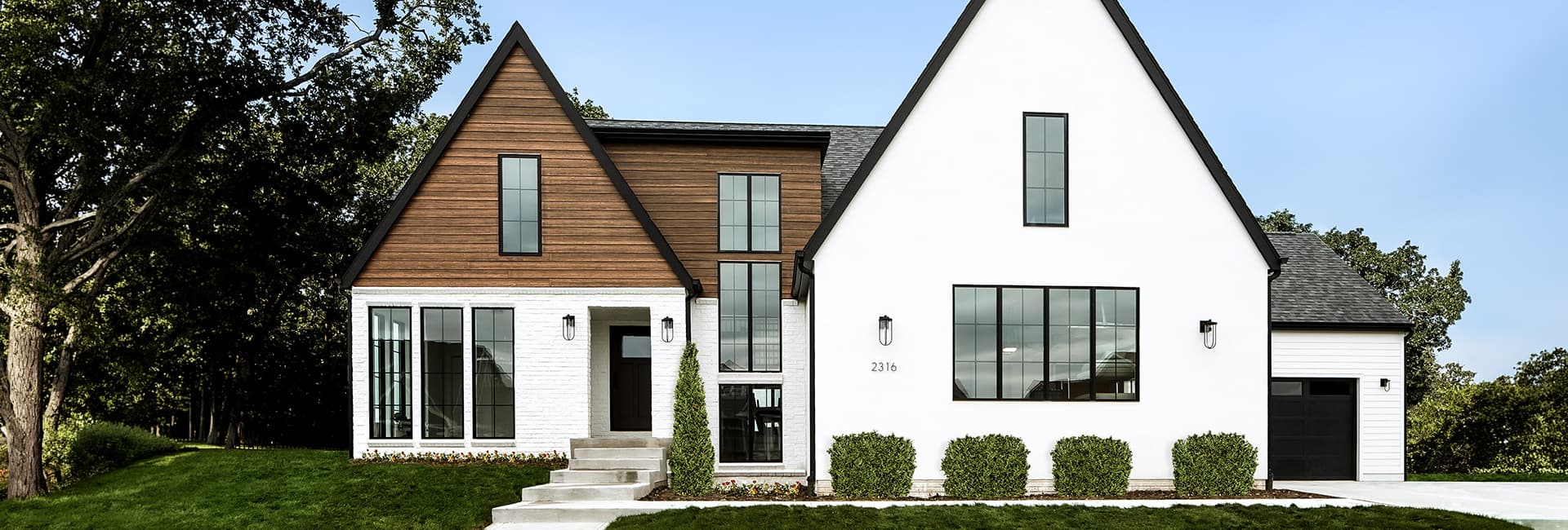 Two-story modern farmhouse front exterior with white stucco and wood siding, black-framed windows, gabled roof, attached garage and landscaped lawn