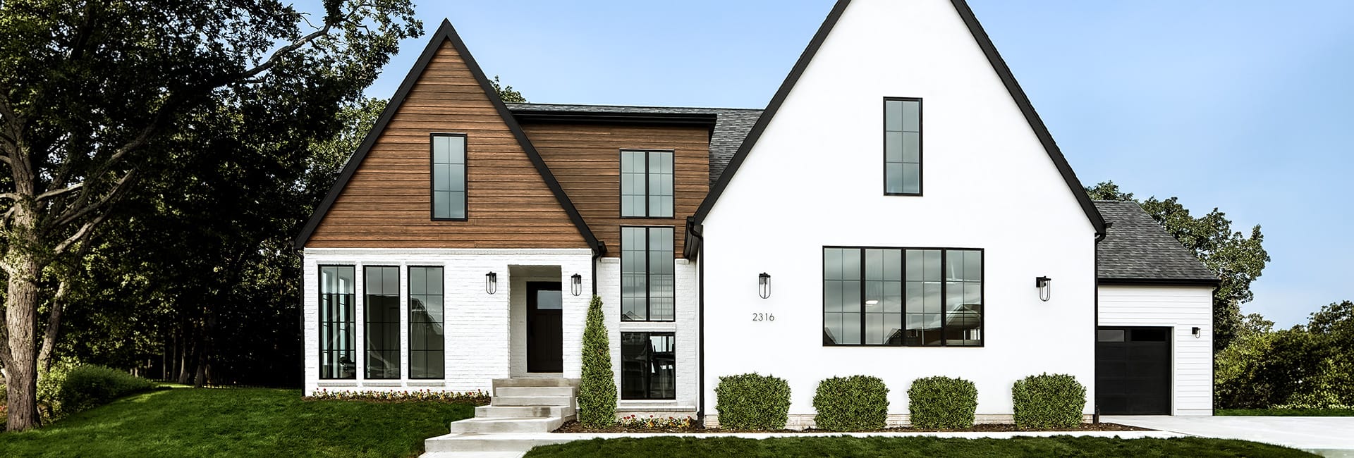 Two-story modern farmhouse front exterior with white stucco and wood siding, black-framed windows, gabled roof, attached garage and landscaped lawn