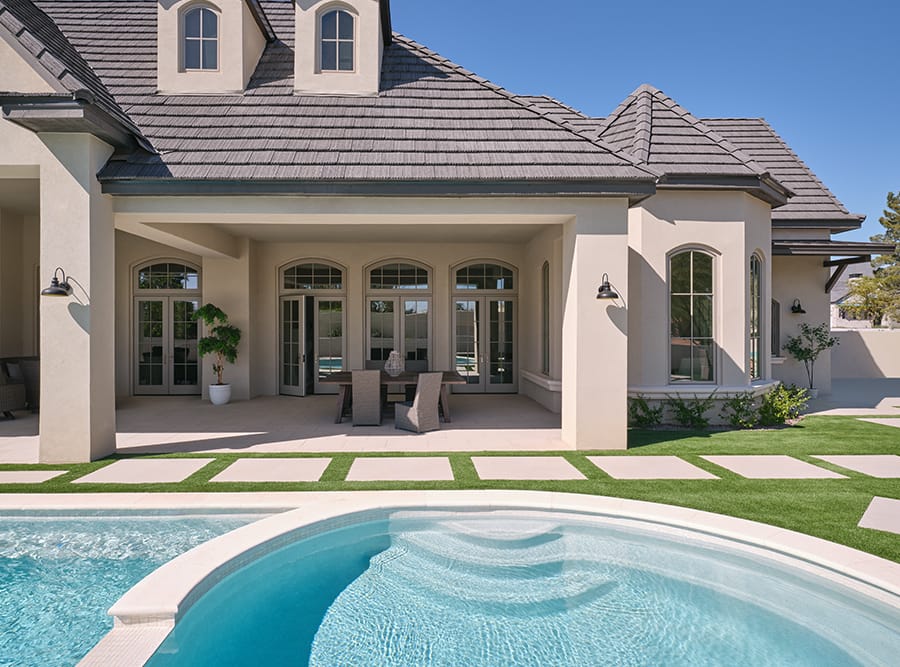 three sets of hinged doors open to an exterior patio that sits between the home and an outdoor pool