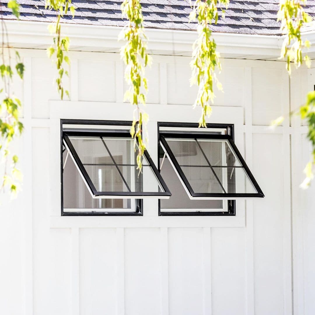 Awning Windows Provide Ventilation for Modern Farmhouse white siding with two black awning windows open and tree limbs hanging down
